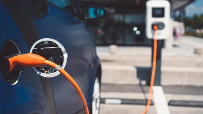 Electric car plugged into a curbside charging station with an orange charging cable